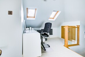 A modern office space with a white desk, black office chair, and two skylights.