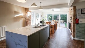A modern kitchen with a marble countertop, pendant lights, and a view to an outdoor dining area. - Meadowfields (Whitby)