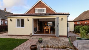 A single-story house with a tiled roof, a patio with a table and chairs, and a garden area with potted plants. - Meadowfields (Whitby)