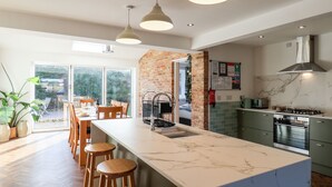 A modern kitchen with a marble island, wooden stools, and a brick accent wall. - Meadowfields (Whitby)