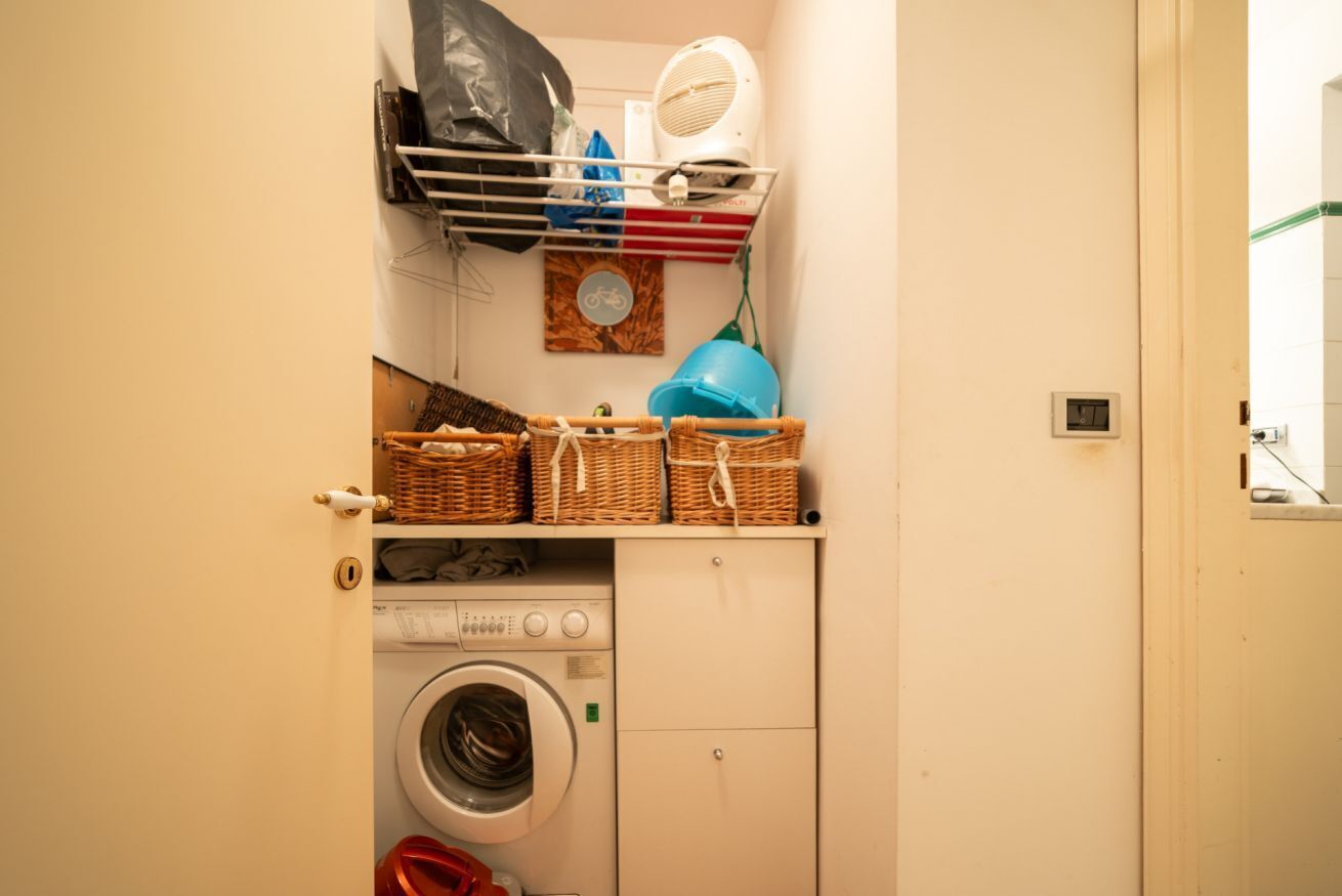 Une petite buanderie équipée d’un lave-linge, de paniers et d’un étendoir.