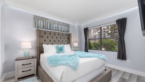 Une chambre à coucher avec un grand lit, deux tables de chevet, une fenêtre avec des rideaux et une tête de lit décorative.