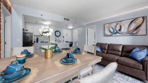 Un espace repas moderne avec une table en bois dressée pour quatre personnes, un canapé en cuir marron et une œuvre d’art abstraite accrochée au mur.