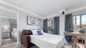Une chambre moderne avec un lit, un canapé marron, un bureau avec une chaise et une grande fenêtre avec des rideaux.
