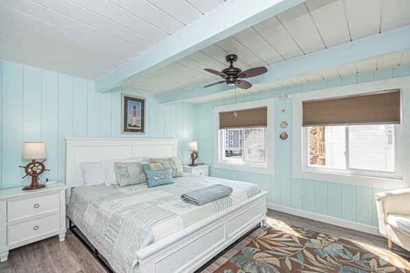 A bedroom with a bed, nightstands, a ceiling fan, a window with blinds, and a view of the outside. - Beautiful Direct Ocean Front Townhome in Sea Village with Relaxing Ocean Views! (Ocean City)
