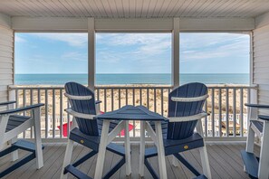 A covered deck with a table and two Adirondack chairs, overlooking a beach. - Beautiful Direct Ocean Front Townhome in Sea Village with Relaxing Ocean Views! (Ocean City)