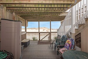 Un espacio al aire libre techado con terraza de madera, vistas a la playa y mobiliario exterior.