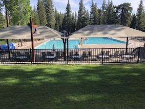 A swimming pool with a fenced area, surrounded by chairs and umbrellas, set in a wooded area. - Luxury Northstar Ski Cabin • Free Shuttle to Lifts • Fireplace • Xbox • Hot Tub (Truckee)