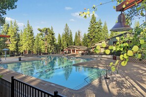 A swimming pool with clear water, surrounded by trees and a building with a sloped roof.