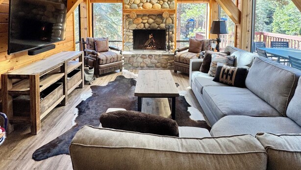 A cozy cabin interior with a stone fireplace, wooden beams, a large TV, and a sofa. - Sleeps 8 • 3BR • Lux Northstar • Free Shuttle • Fireplace • Xbox • Gym • Hot Tub (Truckee)