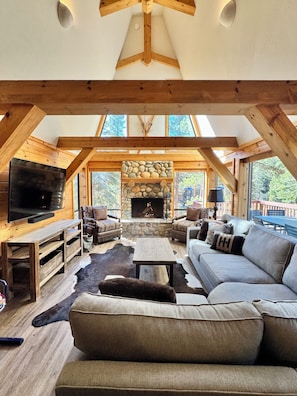 A cozy cabin interior with a stone fireplace, wooden beams, a large TV, and a sofa. - Sleeps 8 • 3BR • Lux Northstar • Free Shuttle • Fireplace • Xbox • Gym • Hot Tub (Truckee)