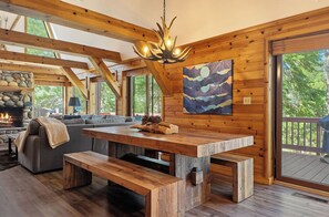 A rustic interior with a stone fireplace, wooden beams, a large table, and a bench.