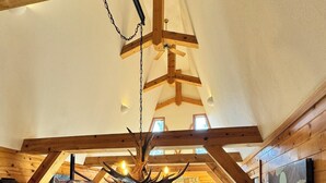 A spacious loft-style living area with a high ceiling, exposed wooden beams, a stone fireplace, and a large window providing natural light. - Sleeps 8 • 3BR • Lux Northstar • Free Shuttle • Fireplace • Xbox • Gym • Hot Tub (Truckee)
