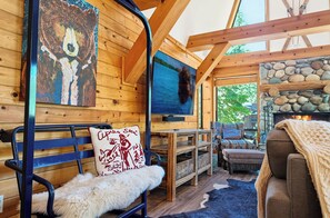 A cozy cabin interior with a stone fireplace, wooden walls, a television, and a bench with a fur throw.