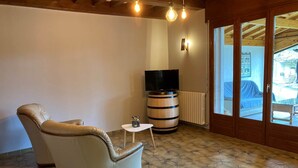 A room with a leather armchair, a small table, a barrel, a television, and a wooden ceiling.