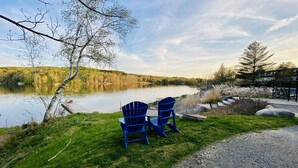 Une vue sur le lac, avec deux chaises Adirondack bleues disposées face à l’eau, entourées de verdure et sous un ciel dégagé.