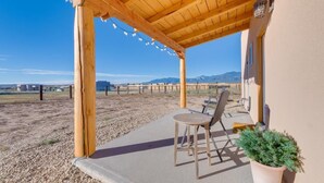 Un porche cubierto con una pérgola de madera, piso de concreto y una zona de estar con mesa y sillas.