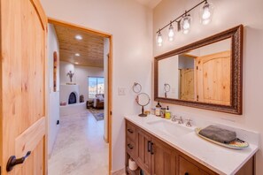 A bathroom with a large mirror, wooden cabinets, and a vanity. - Charming free standing Casita in Taos, NM  (Ranchos de Taos)
