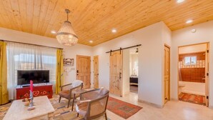 Amplia sala de estar con techo de madera, un candelabro, televisor y comedor con mesa y sillas.