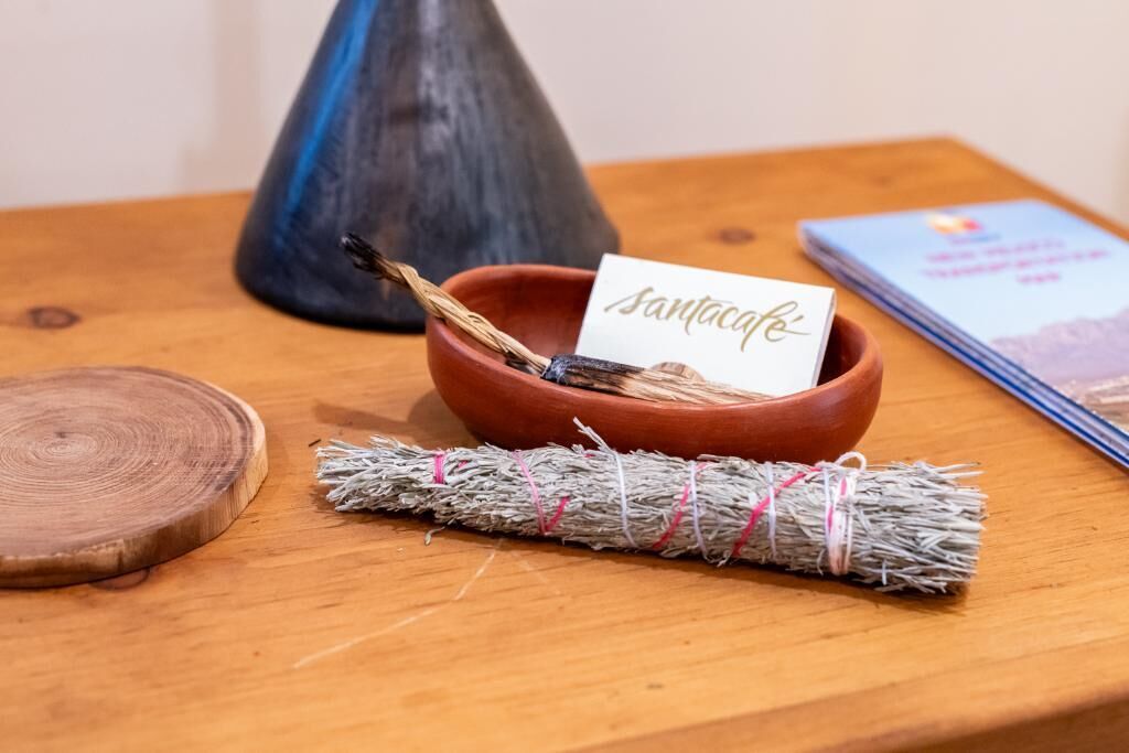Ein Holztisch mit einer braunen Schale, die ein Bündel Zweige, ein mit 'santacruz' beschriftetes Papier und ein Buch mit dem Titel 'SANTACRU' enthält.