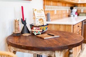 A wooden table with a coffee bag, a ceramic bowl, a red candle, and a notebook. - Charming free standing Casita in Taos, NM  (Ranchos de Taos)