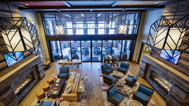 A spacious lobby with a fireplace, comfortable seating, and large windows offering a view of the outdoor area. - The Inn at SentryWorld (Stevens Point)