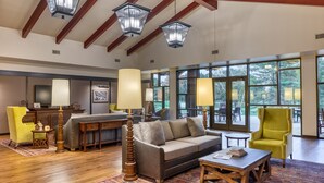 A spacious living room with a sofa, armchairs, a coffee table, and a fireplace. Large windows provide a view of the outdoors. - The Inn at SentryWorld (Stevens Point)