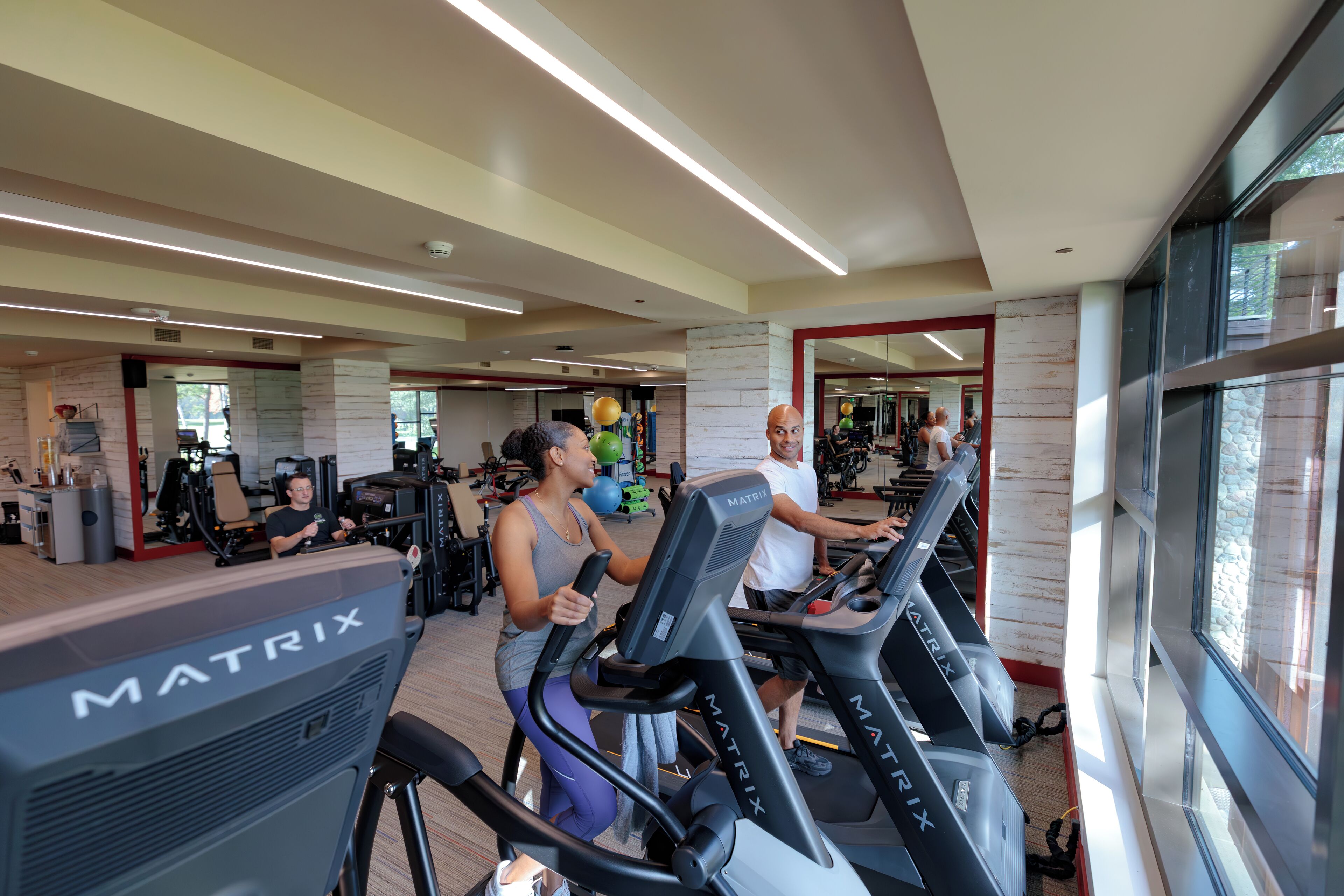 Ein Fitnessstudio mit Laufbändern, Trainingsgeräten und einem großen Spiegel.