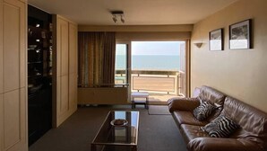 A living room with a leather sofa, a glass coffee table, and a view of the beach. - Amazing 2-bedroom Apartment With Amazing Sea-view (Ostend)