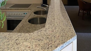 A kitchen with granite countertops, stainless steel sinks, and a built-in oven. There is a coffee maker and a dining area visible in the background. - Amazing 2-bedroom Apartment With Amazing Sea-view (Ostend)