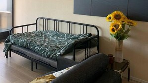 A modern bedroom with a bed, a sofa, a vase with sunflowers, and a large painting on the wall. - Stunning 1-bed Apartment in Oostende Beach-view (Ostend)