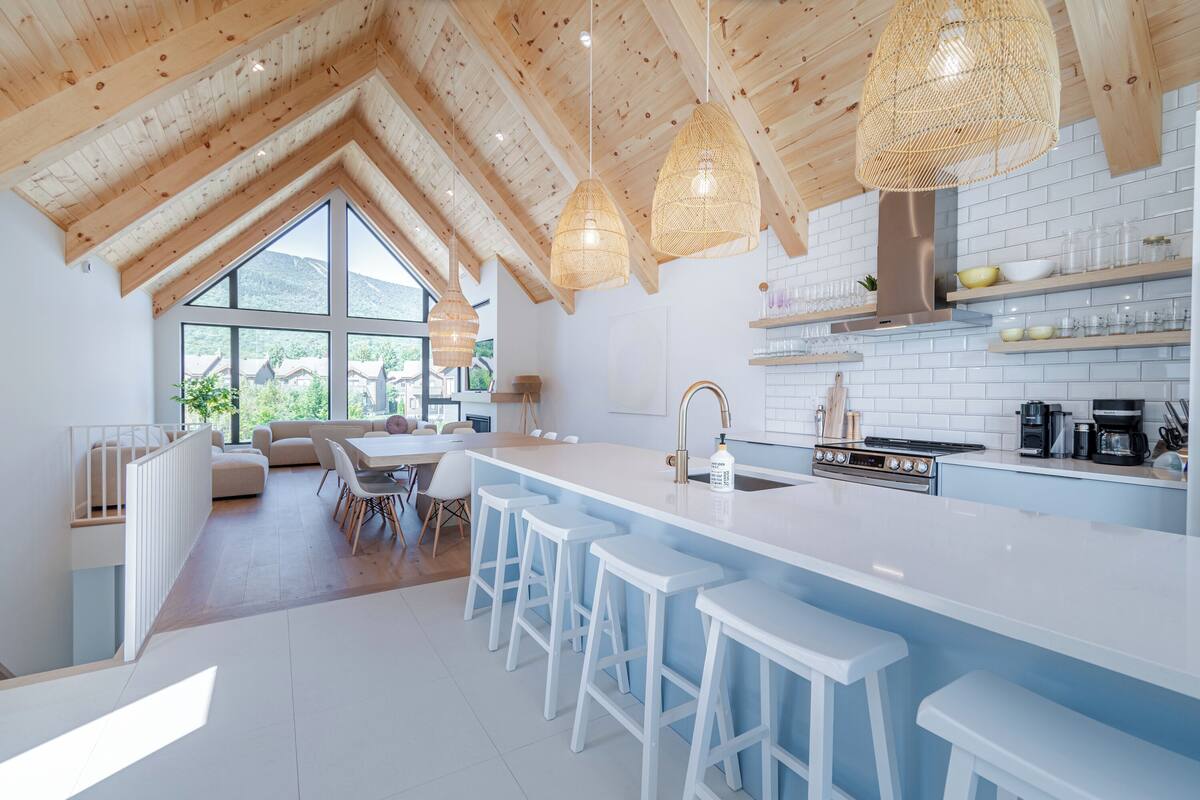 A modern kitchen with a large island, white bar stools, and a view of the outdoors.