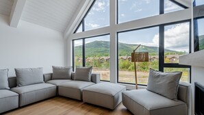 Una sala moderna con un sofá seccional, ventanas amplias que ofrecen vistas a un paisaje montañoso y suelo de madera.