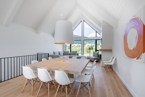 Et rummeligt værelse med et stort træbord omgivet af hvide stole, et moderne loft med ovenlys og et stort abstrakt maleri på væggen.