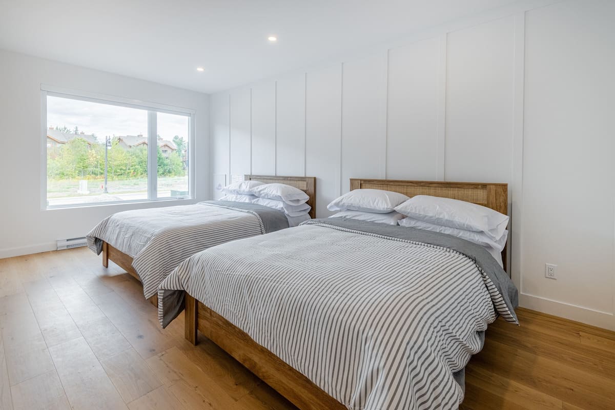 A bedroom with two beds, large windows, and wooden flooring.