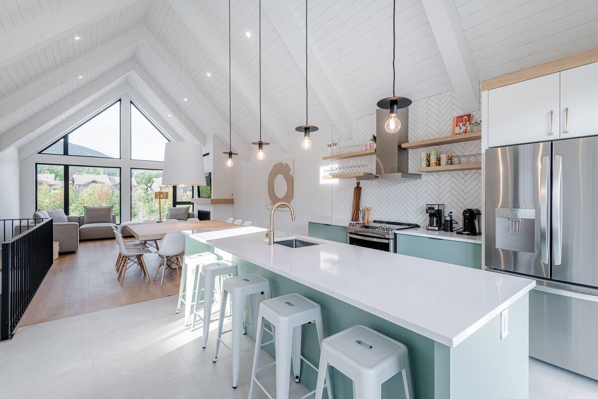 A modern kitchen with a large island, stainless steel appliances, and a dining area with a view.