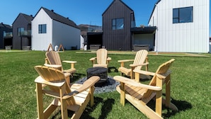 Un área residencial moderna con varias casas, un césped y sillas de madera dispuestas alrededor de un brasero.