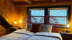 Ein gemütliches Blockhaus-Schlafzimmer mit einem großen Bett, zwei Nachttischen und einem Fenster mit Blick auf Bäume.