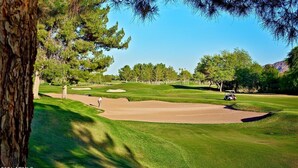 Un campo da golf con bunker di sabbia, alberi e cielo sereno.