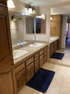 Une salle de bain avec deux lavabos, des meubles en bois, un grand miroir et un tapis de bain bleu.