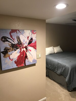 Une chambre à coucher avec un lit, un tableau abstrait accroché au mur et un luminaire au plafond.