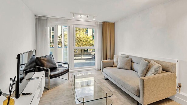 Una sala de estar moderna con un sofá, una silla, una mesita de centro de vidrio y un televisor.