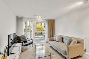 A modern living room with a sofa, a chair, a glass coffee table, and a TV. - City Relay Urban Charm Chelsea Apartment (London)