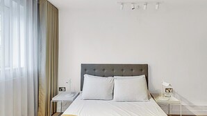 Una habitación de hotel con una cama, dos mesitas de noche, una lámpara y una ventana con cortinas.