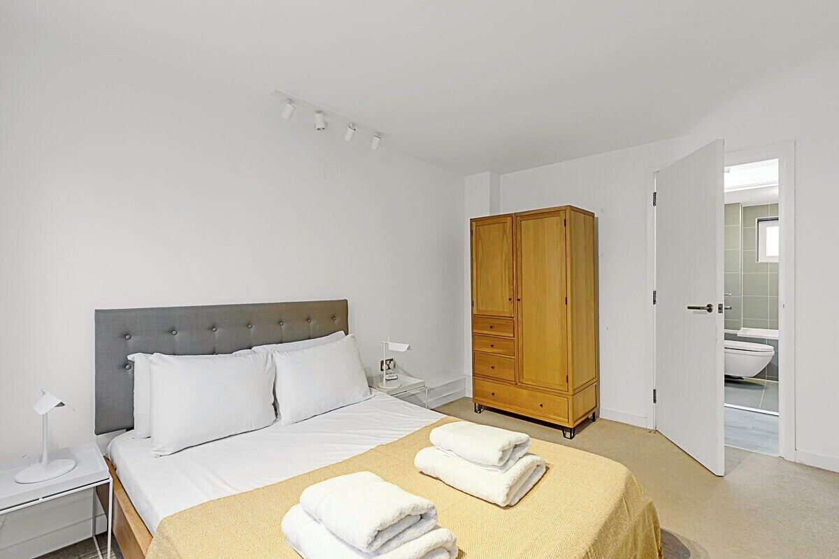 Ein ordentlich eingerichtetes Schlafzimmer mit Bett, Nachttischen, einem Kleiderschrank und einer offenen Tür zu einem Badezimmer.