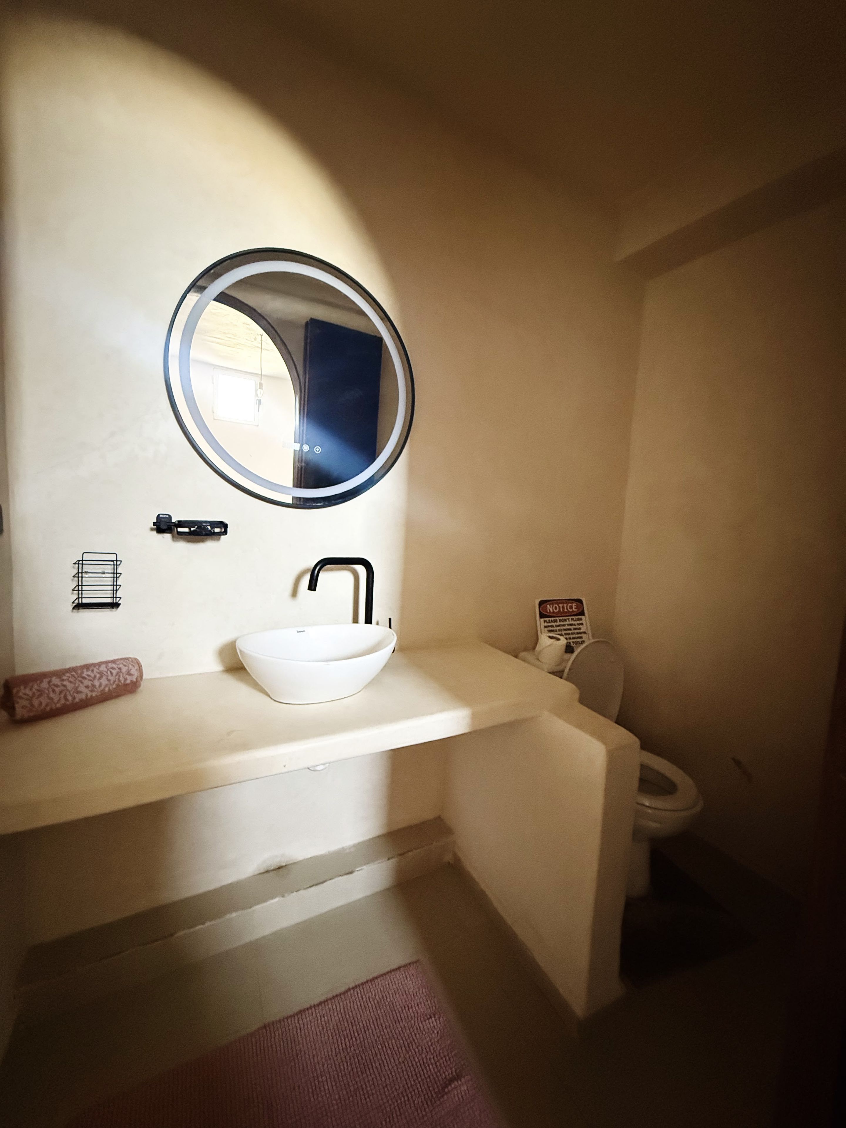Un baño con un espejo redondo, un lavamanos blanco y un inodoro.