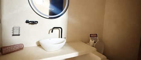 Un baño con un espejo redondo, un lavamanos blanco y un inodoro.