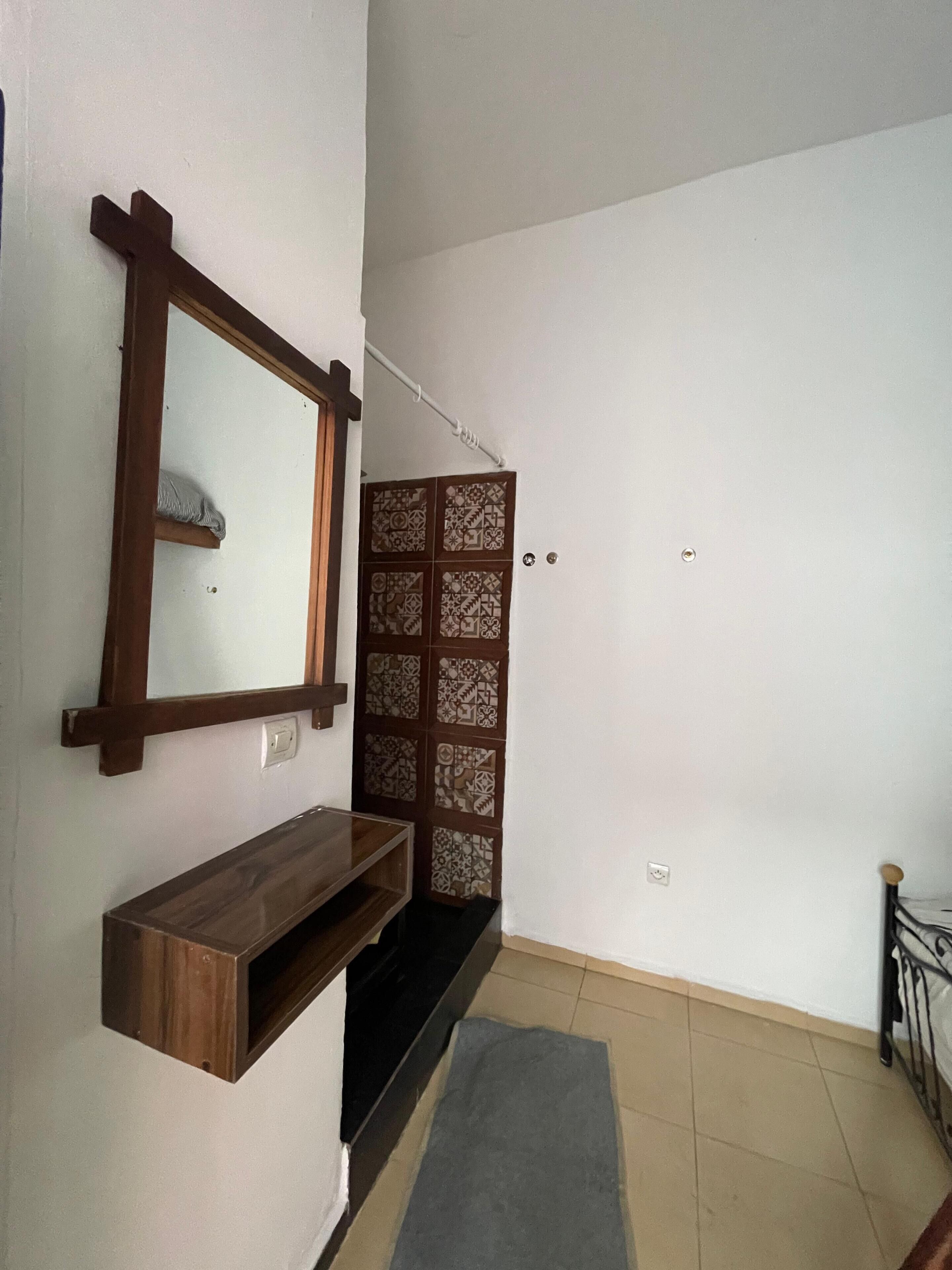 A hallway with a wooden bench, a wall-mounted mirror, a patterned door, and a metal railing.
