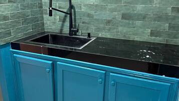 Una cocina con gabinetes azul verdoso, una encimera negra y un lavamanos con grifo negro.
