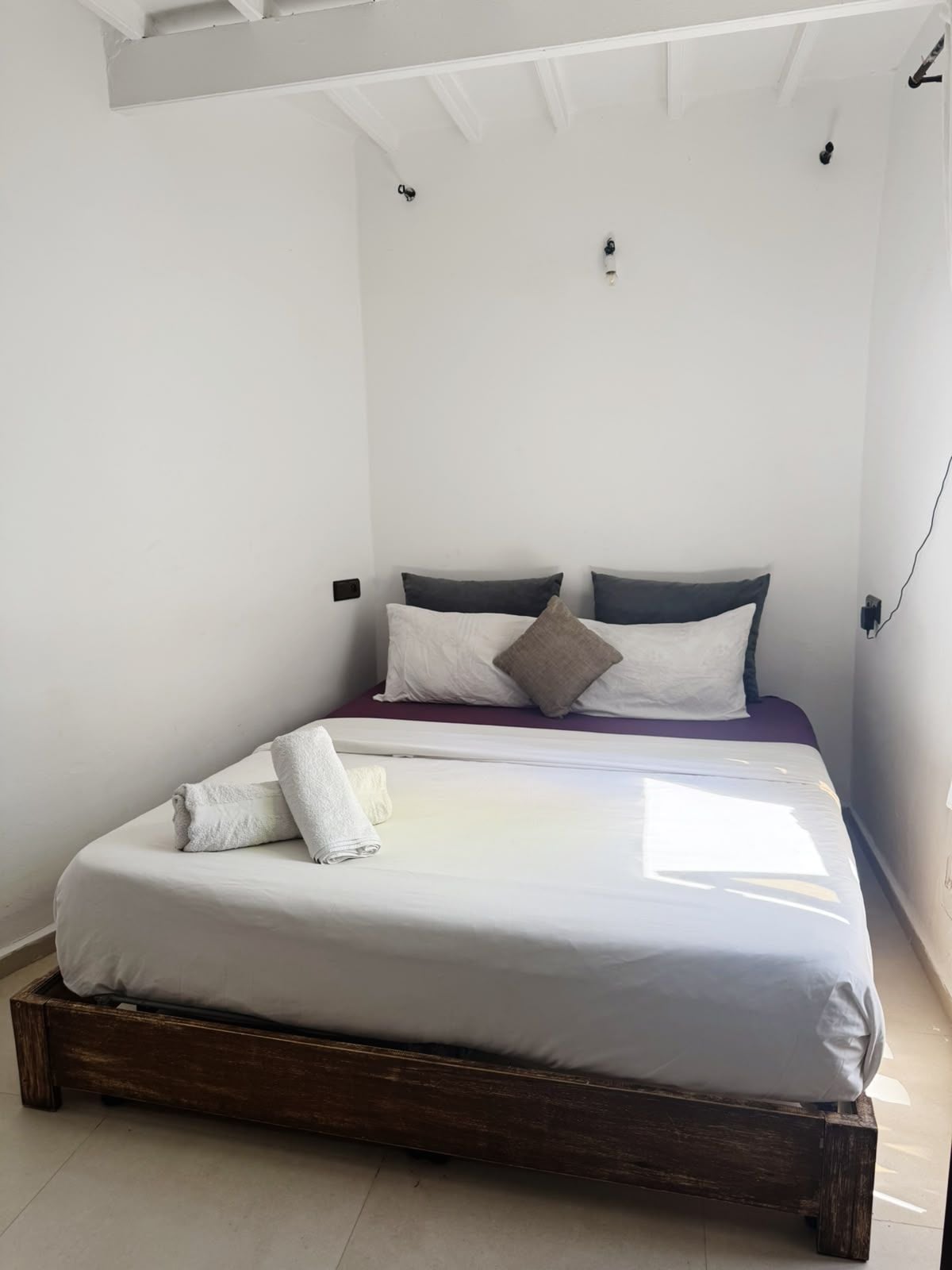A single bed with a wooden frame, white bedding, and two pillows.